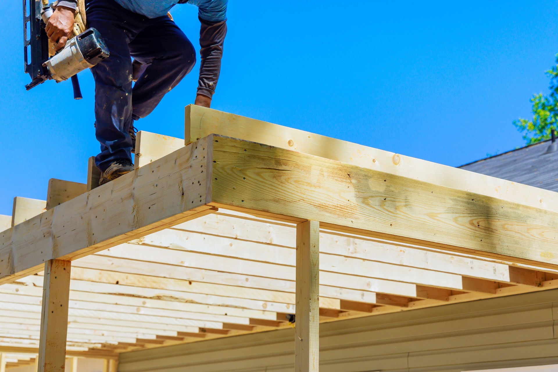 In nailing wooden plank frame together, a framer worker uses an air nails hammer to install beams