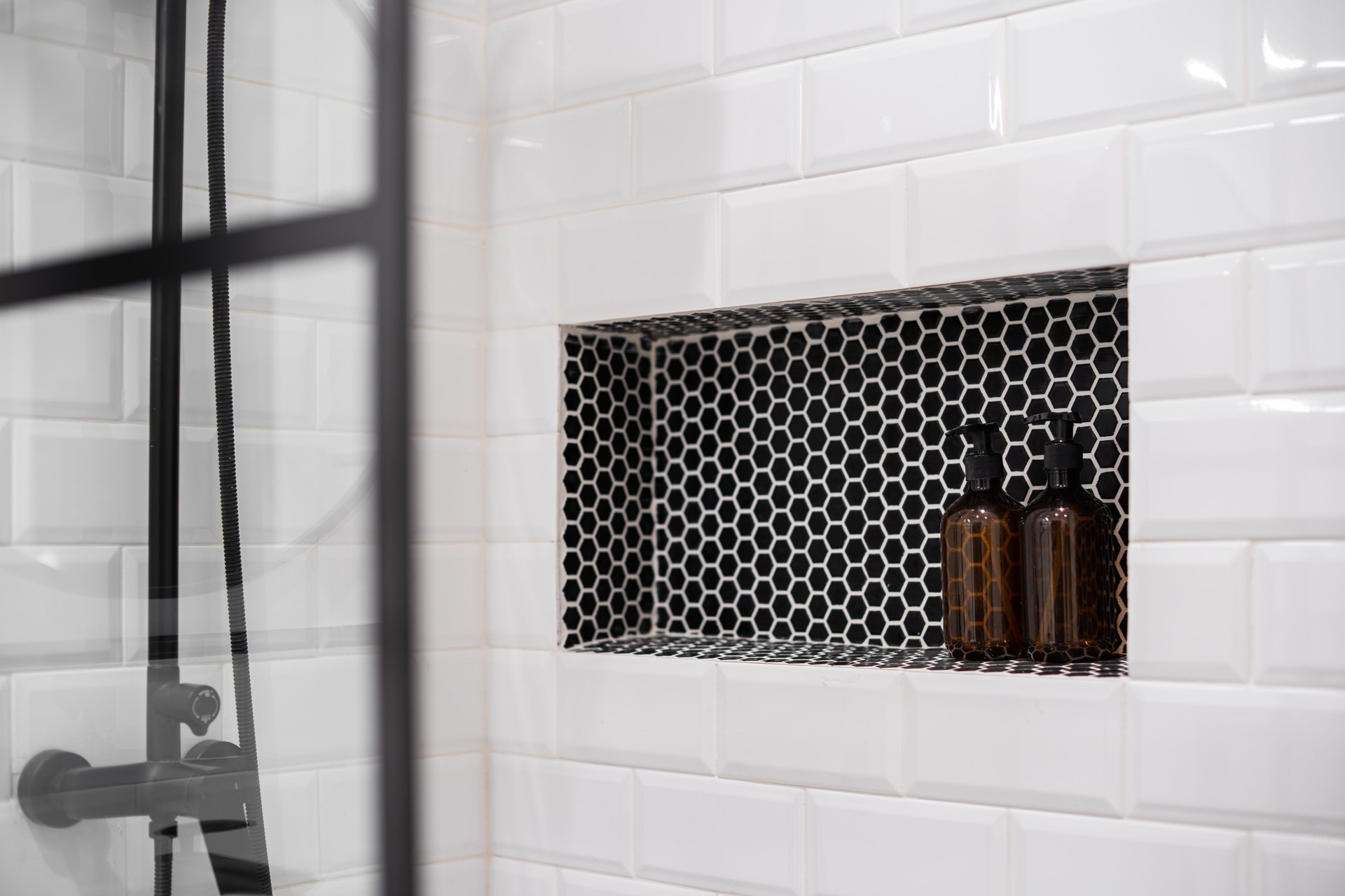 Built-in shelf with bottles in modern bathroom. Shower wall with white tiles.